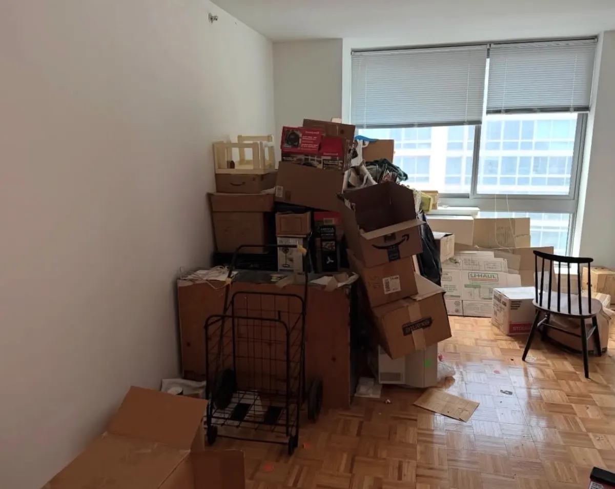 Apartment room before cleanout, stacked with moving boxes, a shopping cart and furniture