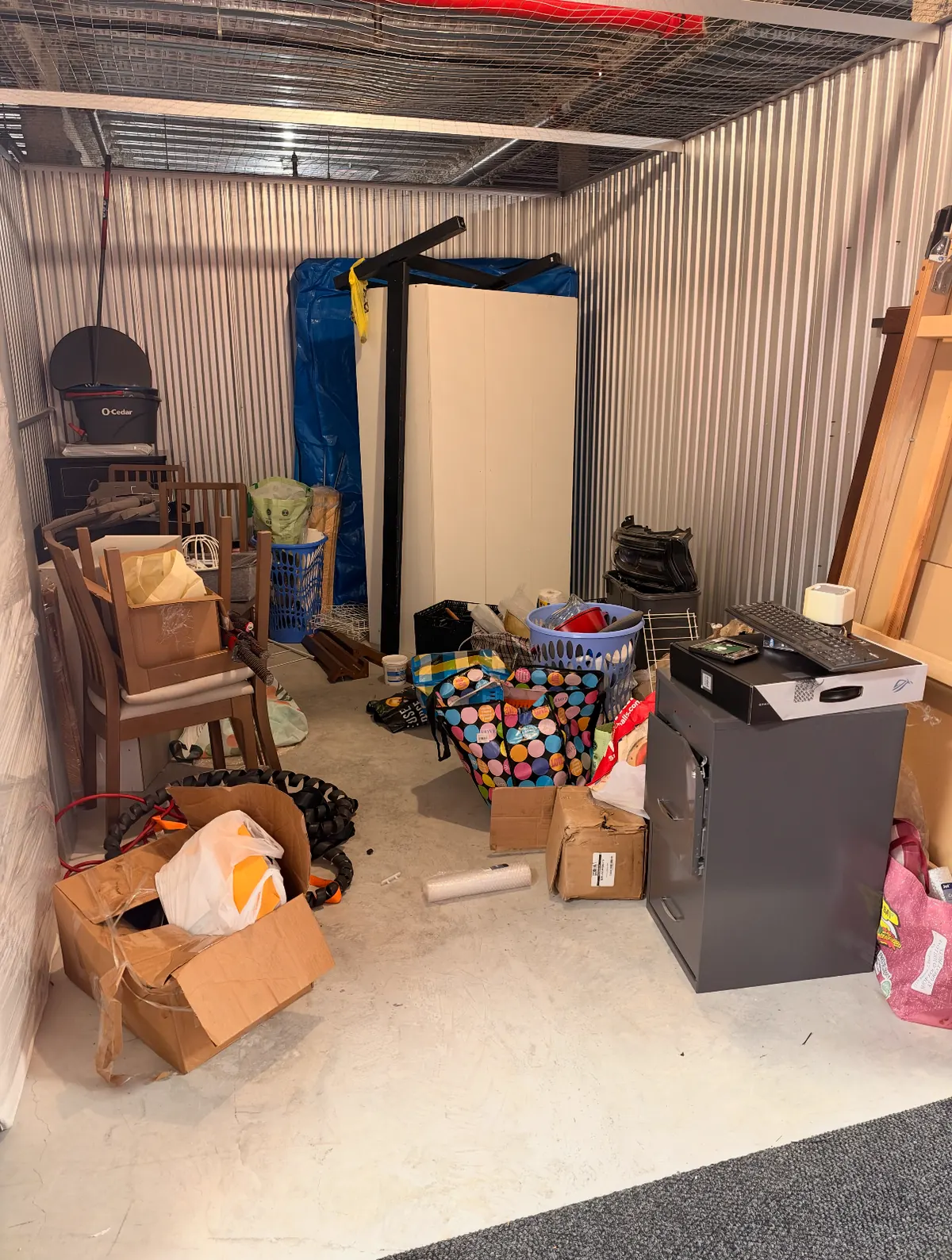 Storage unit filled with chairs, boxes, bags and a filing cabinet, ready to be cleared out